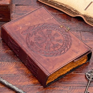 May include: A brown leather-bound journal with a compass and dragon design embossed on the cover. The journal has a clasp closure and is made of high-quality leather.