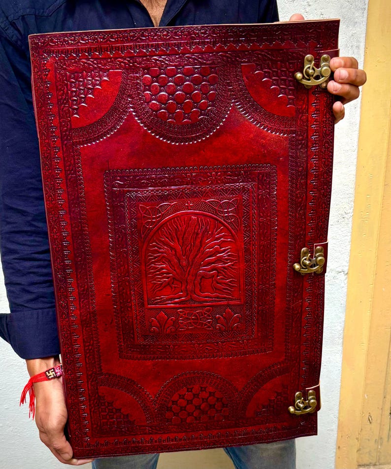 Pode incluir: Um grande di&aacute;rio retangular de couro vermelho com intrincados desenhos em relevo. A capa apresenta um motivo central de &aacute;rvore e bordas decorativas. O di&aacute;rio &eacute; preso com fechos e dobradi&ccedil;as de lat&atilde;o, sugerindo um estilo vintage ou artesanal.