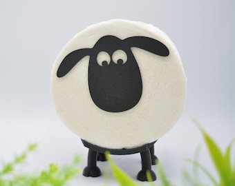 May include: A white sheep-shaped object with black paper cutouts for the face, ears, and legs. The sheep is standing on a white surface.