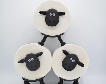 May include: Three black and white sheep toilet paper holders stacked on top of each other. The sheep have black eyes and noses and white wool.