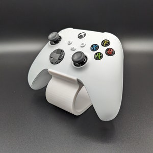 Può includere: Un controller Xbox bianco con pulsanti neri e un supporto bianco. Il controller ha un logo Xbox verde sul davanti.
