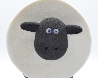 May include: A white sheep with a black face and googly eyes. The sheep is made of foam and has a textured surface.