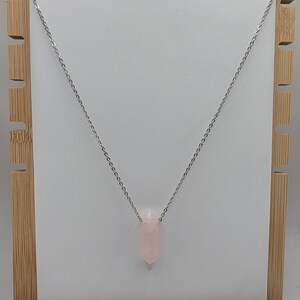Könnte beinhalten: Eine silberne Kettenkette mit einem Anhänger aus hellrosa Rosenquarz. Der Anhänger ist spitz zulaufend.