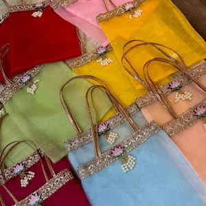 Op de afbeelding: Een verzameling kleurrijke, transparante draagtassen in de kleuren rood, roze, geel, groen, blauw en perzik. Elke tas heeft een decoratieve gouden rand, een bloemversiering en een handvat.