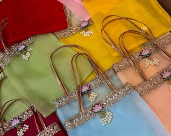 May include: A collection of colorful, sheer tote bags in shades of red, pink, yellow, green, blue, and peach. Each bag features a decorative gold trim, a floral embellishment, and a handle.