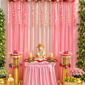 May include: A decorative display featuring a central white Ganesha statue on a pink draped table, flanked by two gold pillars topped with pink and white floral arrangements. A pink curtain backdrop is adorned with hanging floral garlands.