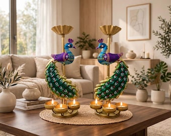 May include: Two gold-toned metal candle holders featuring decorative peacock figures with blue, purple, and green painted details. Each stand supports a top candle cup and three lower circular candle holders, all containing lit tea light candles.