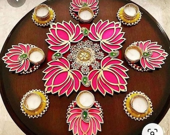 May include: A decorative diya set with eight pink lotus flower designs and eight yellow candle holders. The diyas are arranged in a circle on a dark brown wooden surface.