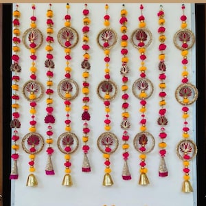 May include: Nine decorative door hangings with gold bells and tassels. Each hanging features a circular design with a lotus flower cutout and alternating pink and yellow pom-poms.
