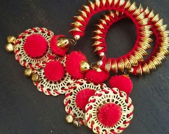 May include: Red and gold-colored jewelry set. The set includes two spiral-shaped bangles with gold accents and several matching earrings with red pom-poms and gold filigree detailing. Small gold bells hang from the earrings.