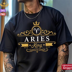 Op de afbeelding: Zwart T-shirt met een goud en wit Aries King ontwerp. Het ontwerp bevat het Ram-symbool, een kroon en de woorden "ARIES" en "King". Het shirt heeft korte mouwen en een ronde hals.