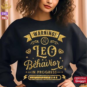 May include: A black long-sleeve sweatshirt featuring a gold glitter graphic design. The text reads WARNING! LEO BEHAVIOR IN PROGRESS, accompanied by a Leo zodiac symbol, diamond icons, and a loading bar graphic, all rendered in a sparkling gold texture.