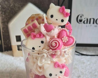 Könnte beinhalten: Eine rosa und weiße Kerze im Hello-Kitty-Design in einem Glasgefäß. Die Kerze ist mit Hello-Kitty-Figuren, Herzen und anderen süßen Leckereien verziert. Das Gefäß trägt ein Etikett mit der Aufschrift "CandlelitWishes' Kitty Kingdom".