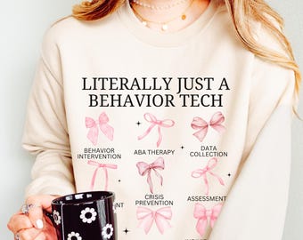 May include: A beige sweatshirt with the text "LITERALLY JUST A BEHAVIOR TECH" printed on the front. The text is surrounded by pink bows with different text underneath each bow, including "Behavior Intervention", "ABA Therapy", "Data Collection", "Crisis Prevention", "Assessment", "Prompting & Fading".