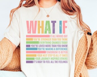 May include: A cream-coloured t-shirt featuring the phrase "WHAT IF" in a distressed, multi-coloured font. Beneath, a series of positive affirmations in different colours. A casual, everyday garment.