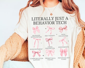 May include: White t-shirt with the text "LITERALLY JUST A BEHAVIOR TECH" and a graphic of pink bows representing different aspects of behaviour therapy, including behaviour intervention, ABA therapy, data collection, reinforcement, crisis prevention, assessments, communication support, prompting & fading, and individualized plans.