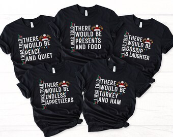 May include: Five black t-shirts with a Christmas theme. Each shirt has a different saying with the text "I was told" and a Christmas light design. The sayings are "There would be peace and quiet", "There would be endless appetizers", "There would be presents and food", "There would be turkey and ham", and "There would be gossip and laughter".
