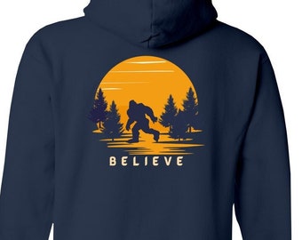 May include: Navy blue hooded sweatshirt with a graphic of a Bigfoot walking in front of a yellow sunset with trees. The text "BELIEVE" is printed below the graphic.