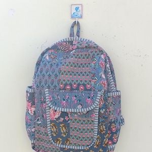 May include: A gray patchwork backpack with floral patterns in pink, blue, and green. The backpack has a large front pocket and adjustable straps.