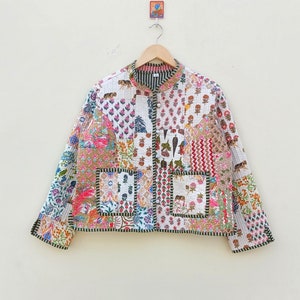 Puede incluir: Una chaqueta acolchada blanca con un diseño de patchwork que presenta varios patrones florales y geométricos en tonos de rosa, azul, verde y marrón. La chaqueta tiene un cuello mandarín, cierre de botón y dos bolsillos de parche.