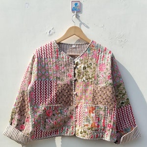 May include: A patchwork quilted jacket with a floral print in shades of pink, red, brown, and white. The jacket has a button closure and two patch pockets.