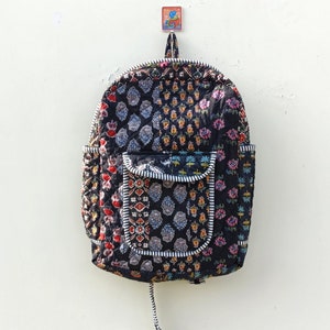 Può includere: Uno zaino nero trapuntato con un design patchwork con motivi floreali colorati. Lo zaino ha una grande tasca frontale con un bordo bianco.