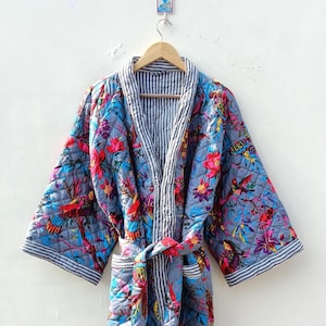Könnte beinhalten: Eine blaue gesteppte Robe mit einem Blumen- und Vogelmuster. Die Robe hat ein weiß-blaues gestreiftes Futter und einen passenden Bindegürtel.