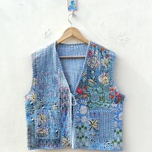May include: A blue quilted vest with a floral print and a V-neck. The vest has a zip closure and two pockets.