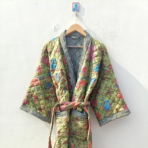 Op de afbeelding: Een groene gewatteerde badjas met een bloemenprint en een zwart-wit gestreepte voering. De badjas heeft een strikceintuur en lange mouwen.