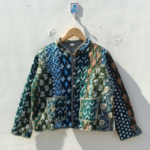 May include: A green quilted jacket with a patchwork design featuring various floral and geometric patterns in shades of blue, green, and orange. The jacket has a button closure and two pockets.