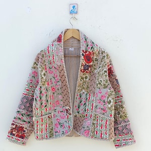 Könnte beinhalten: Eine gesteppte Jacke mit Patchwork-Design mit floralen Mustern in Rosa-, Rot- und Grüntönen. Die Jacke hat einen Kragen und lange Ärmel.