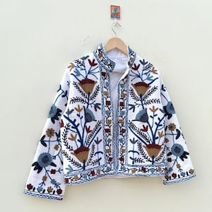 May include: White embroidered jacket with a floral pattern in shades of blue, brown, and red. The jacket has a mandarin collar and a button closure.