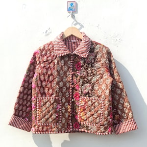 Peut inclure: Une veste matelassée marron avec un imprimé floral et un col rayé blanc et rouge. La veste a deux poches sur le devant et une fermeture à bouton.