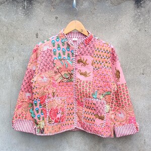 Könnte beinhalten: Rosa Patchwork-Jacke mit Stehkragen und zwei Vordertaschen. Die Jacke hat verschiedene Blumen- und geometrische Muster in Rosa, Koralle und Türkis. Die Manschetten und der Saum sind mit einem gestreiften Stoff versehen.