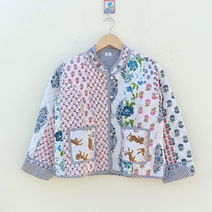 May include: A white quilted jacket with a patchwork design featuring floral and tiger prints. The jacket has a mandarin collar, a button closure, and two patch pockets.