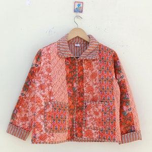 Puede incluir: Una chaqueta acolchada de patchwork en tonos naranja y rosa con estampados florales y geométricos. La chaqueta tiene una cremallera y un cuello.