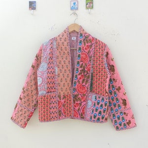 Könnte beinhalten: Eine rosafarbene gesteppte Jacke mit Patchwork-Design, das florale und geometrische Muster zeigt. Die Jacke hat lange Ärmel und einen Kragen.
