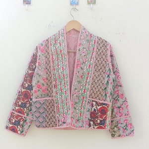 Puede incluir: Una chaqueta acolchada de patchwork con estampado floral en tonos rosa, rojo y verde. La chaqueta tiene un forro a rayas rojo y blanco y un cuello en V.