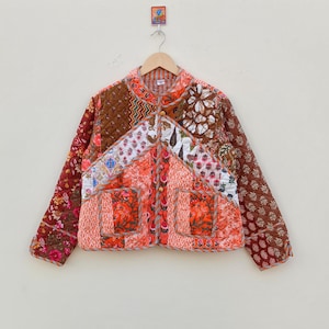 Może przedstawiać: Kurtka pikowana w patchwork z brązowym, pomarańczowym i białym nadrukiem kwiatowym. Kurtka ma kołnierz mandaryński, zapięcie na guziki i długie rękawy.