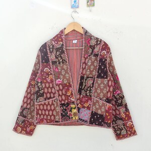 Op de afbeelding: Een bruin gewatteerd jack met een patchwork-ontwerp met bloemenpatronen. Het jack heeft lange mouwen, een V-hals en een knoopsluiting.