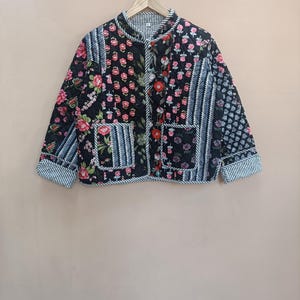 以下が含まれることがあります： 黒いキルティングジャケット。花柄とストライプのアクセントが特徴です。ジャケットはマンダリンカラー、2つのポケット、ボタン留めです。花柄にはピンク、赤、白の花が含まれています。
