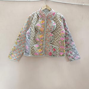 May include: A quilted jacket featuring a patchwork design with various floral and paisley patterns in shades of pink, yellow, and green on a light background. The jacket has a mandarin collar, long sleeves, and a front button closure.