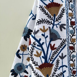 May include: White linen jacket with blue, brown, and red embroidered floral pattern.