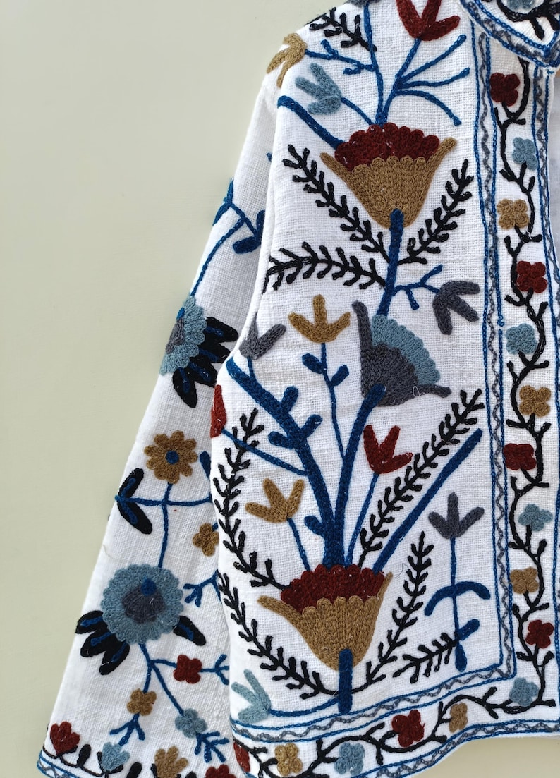 May include: White linen jacket with blue, brown, and red embroidered floral pattern.