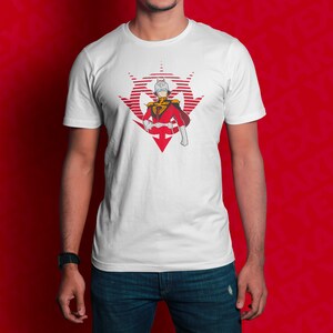 Op de afbeelding: Wit T-shirt met een rode en witte afbeelding van een personage dat een helm en een rood en wit uniform draagt. Het personage staat voor een rood en wit symbool.
