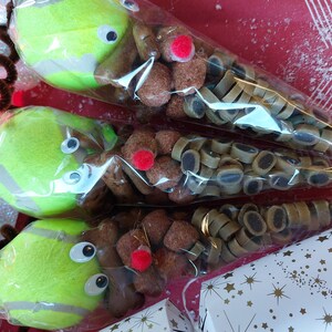May include: Three clear plastic cones filled with dog treats. Each cone has a green tennis ball attached to the top, with googly eyes and a red pom-pom nose. The cones are decorated with brown pipe cleaner antlers.