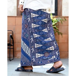 以下が含まれることがあります： 青と白の模様の入ったサロング。花柄のデザインで、白い縁取りと、下部に「Pekalongan」という文字が印刷されています。