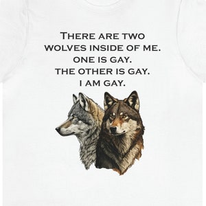May include: White t-shirt with a black graphic print of two wolves and the text "THERE ARE TWO WOLVES INSIDE OF ME. ONE IS GAY. THE OTHER IS GAY. I AM GAY."