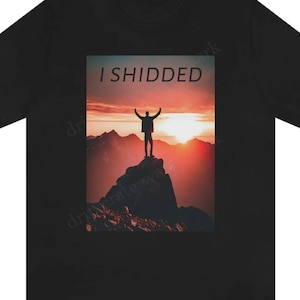 Puede incluir: Camiseta negra con un gráfico rectangular de una persona con los brazos levantados en la cima de una montaña al atardecer. El texto "I SHIDDED" está encima del gráfico en letras blancas. La camiseta es de material suave.