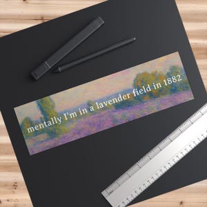 May include: A rectangular bookmark with a lavender field painting and the text "mentally I'm in a lavender field in 1882" in white. The bookmark is on a black surface with a ruler and pen.